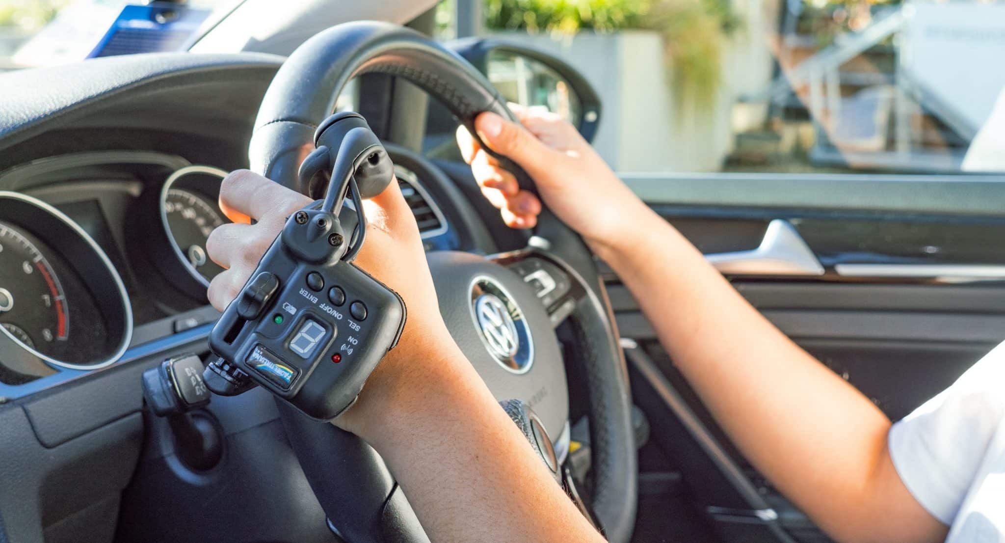 Side view of persons arms holding a steering wheel in driver seat with Satellite Accelerator hand control on left hand