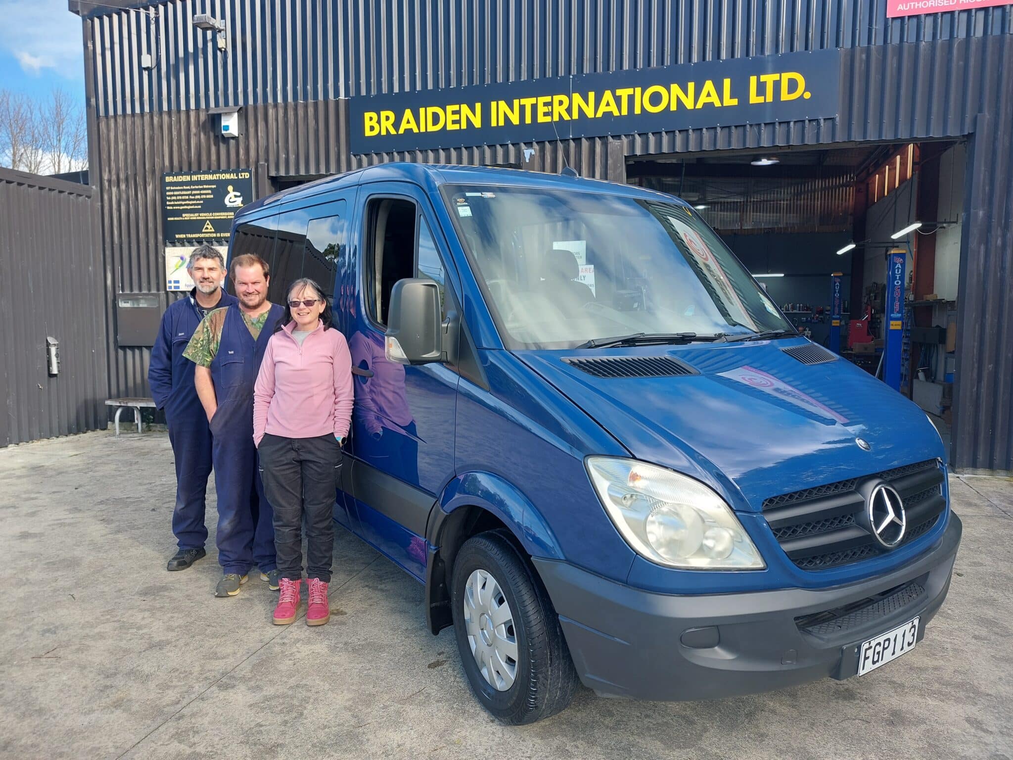 Three team members in front of blue van at Braiden International workshop